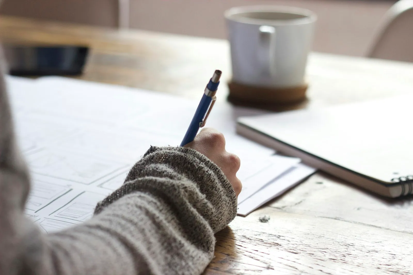 Une personne remplit sereinement un dossier papier à une table en bois, une tasse à portée de main